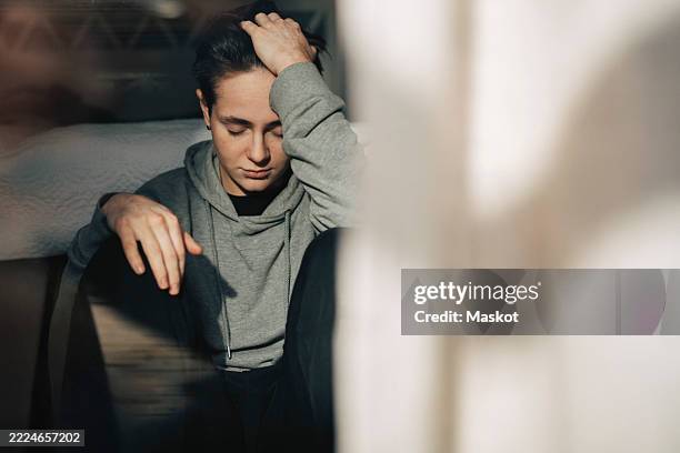 sad young man sitting with hand in hair at home - mal de tête photos et images de collection