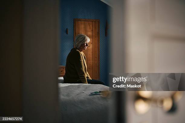 sad elderly woman sitting on bed in bedroom at home - abgeschiedenheit stock-fotos und bilder