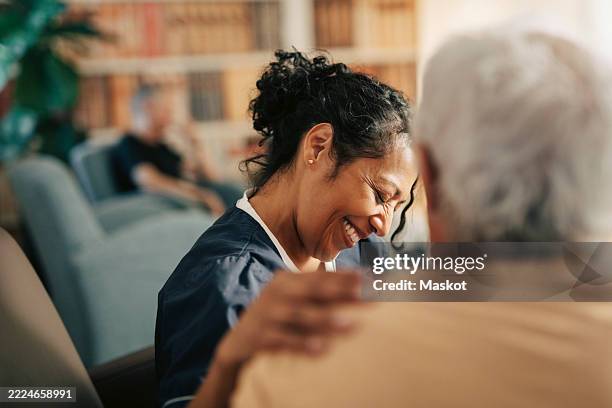 smiling female nursing assistant with hand on shoulder of senior patient at retirement home - krankenschwester stock-fotos und bilder