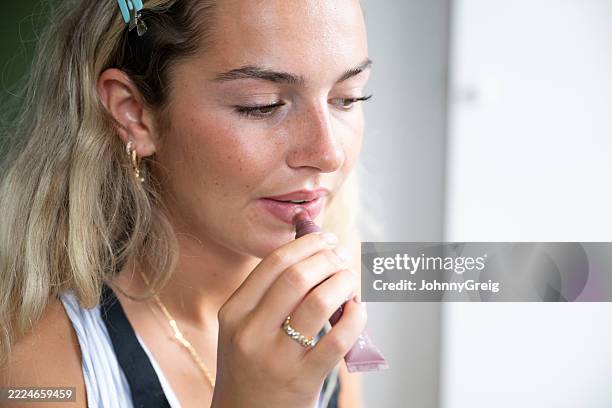 portrait candide en gros plan d’une jeune fille de 19 ans appliquant du brillant à lèvres sur ses lèvres - brillant à lèvres photos et images de collection