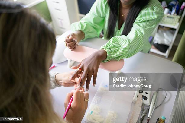 young nail technician applying nail polish to fingernails of teenage girl - manicure stockfoto's en -beelden