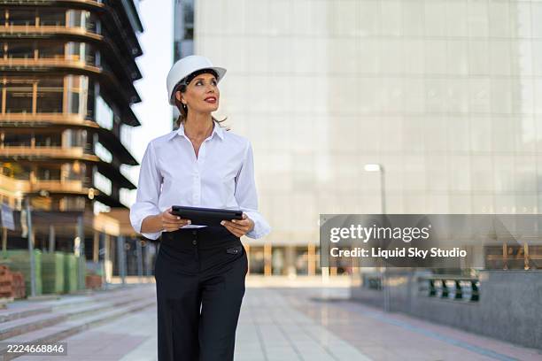 arquitecta caminando con tableta digital - casco de seguridad fotografías e imágenes de stock