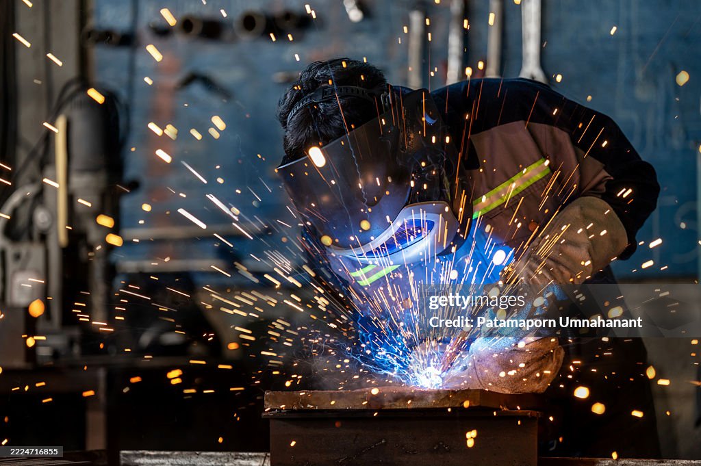 A professional welder wearing full protective gear works with steady hands and focus, welding a metal component. The vibrant sparks create a beautiful bokeh that contrasts the intense environment with artistic energy, showcasing skill and dedication.