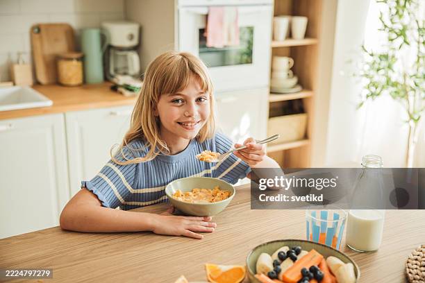 bambina carina che guarda la macchina fotografica mentre mangia cereali - cereali da colazione foto e immagini stock