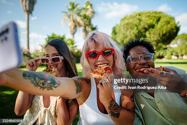 three young friends taking a selfie while eating pizza outdoors - eating pizza stock pictures, royalty-free photos & images