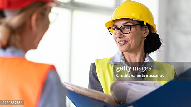 female construction manager wearing helmet and reflective vest while discussing with colleague - human role stock pictures, royalty-free photos & images