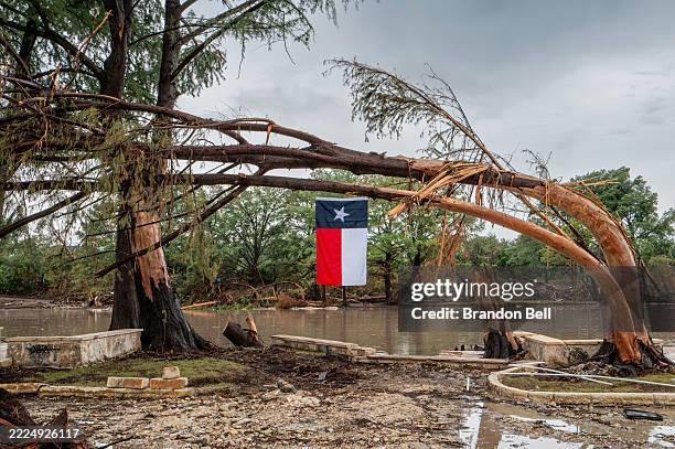 Texas flag hangs from a storm-damaged tree on the banks of the Guadalupe River on July 13, 2025 in Center Point, Texas. More than 160 people are...