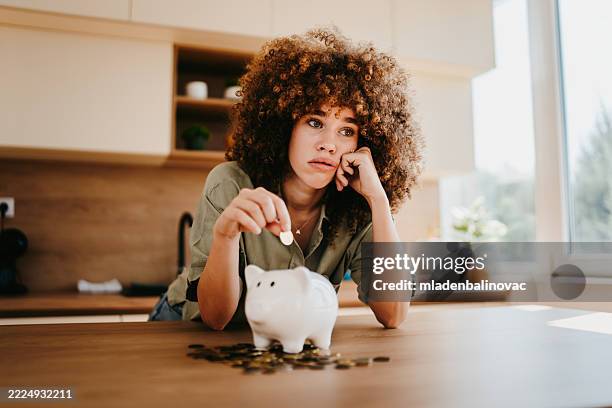 mujer joven ahorrando dinero en la alcancía en la cocina de su casa - adversidad fotografías e imágenes de stock