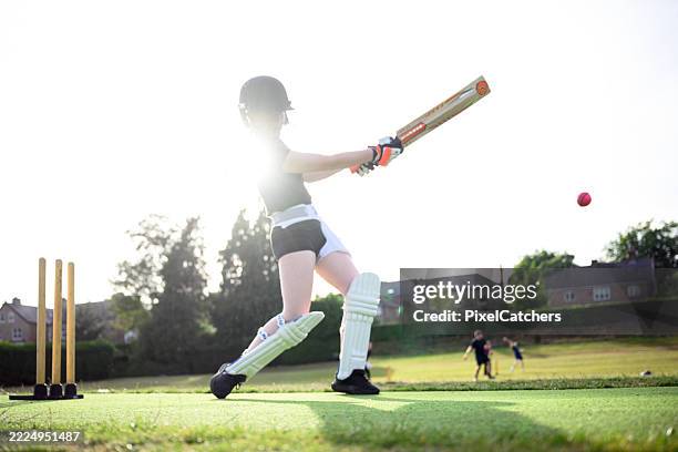 low angle teenage female batsman wearing protective sports wear taking a swing at the ball - cricket bat stock pictures, royalty-free photos & images