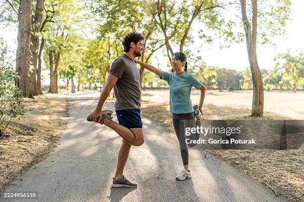 young couple stretching legs together before running in a park - quadriceps muscle stock pictures, royalty-free photos & images