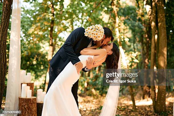 le marié penchant la mariée pour un baiser lors d’une cérémonie de mariage en forêt - cérémonie du mariage photos et images de collection