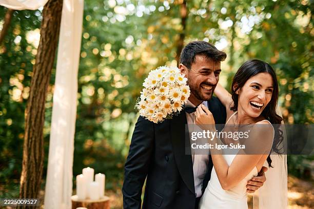 de jeunes mariés heureux riant et s’embrassant dans les bois lors de leur cérémonie de mariage - cérémonie du mariage photos et images de collection