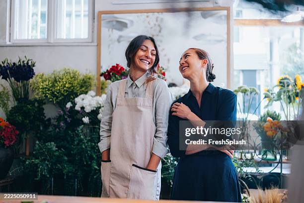 two female florists smiling and chatting in a blooming flower shop - eigenaar stockfoto's en -beelden