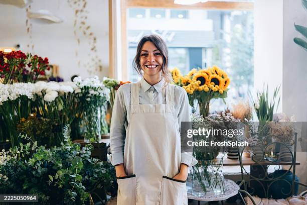 fiorista sorridente in piedi in un negozio di fiori accanto a composizioni in fiore - composizione di fiori foto e immagini stock