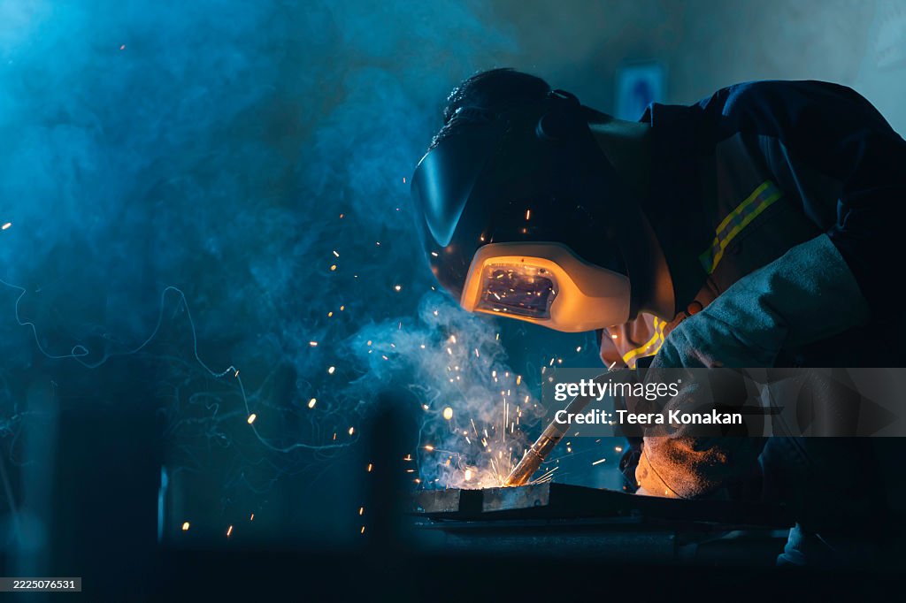 Professional welder wearing a dark helmet and gloves welds steel