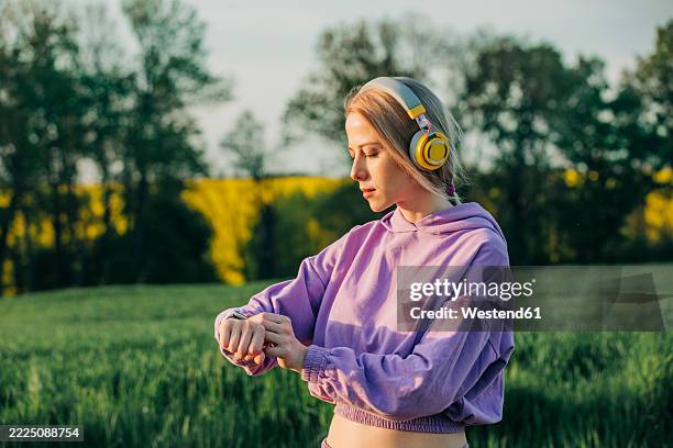 woman in lavender athletic outfit checking pulse with smartwatch while listening to music outdoors - wearable ai stock pictures, royalty-free photos & images