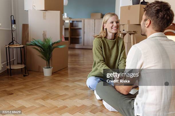 happy young couple sitting on the floor of their new home - parket stockfoto's en -beelden