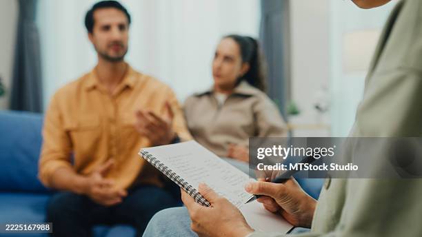nahaufnahme eines jungen paares in ernsthafter diskussion mit einem psychiater während der eheberatungssitzung, die auf dem sofa im wohnzimmer zu hause sitzt. therapiesitzung konzept für psychische gesundheit. - eheberatung stock-fotos und bilder