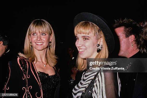British and Australian singer and actress Olivia Newton-John, wearing a black-and-bronze jacket over a sparkling black outfit, and American singer...