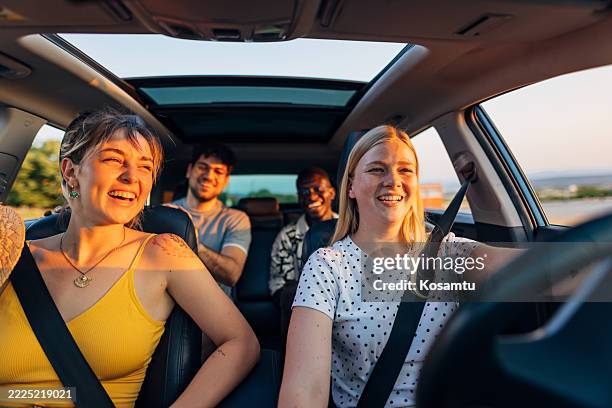 eine sorglose frau fährt auto, während sie mit freunden in den sommerurlaub fährt. die sonne scheint durch die autofenster und unterstreicht die heiße sommeratmosphäre der reise - fahrgemeinschaft stock-fotos und bilder