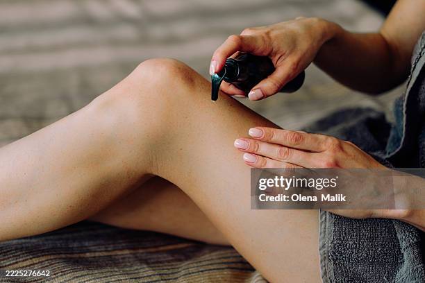 woman applying skin lotion to her leg for nourished and smooth skin - aceite de masaje fotografías e imágenes de stock