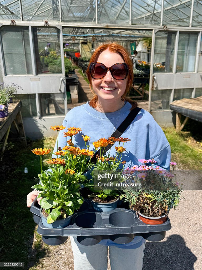 Image of girl shopping for annual spring flowers and flowering plants, holding pots of vibrant orange daisy Osteospermum