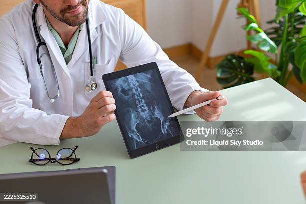 un médecin montre une radiographie pelvienne sur tablette à un patient dans un cabinet médical - hanche photos et images de collection