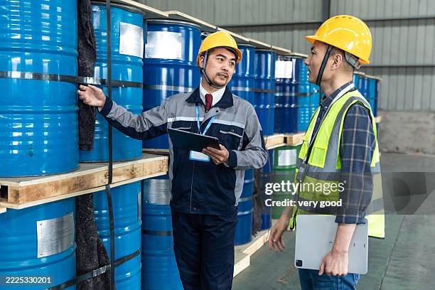 two asian male examining & discussing in chemicals warehouse - brennbar stock-fotos und bilder