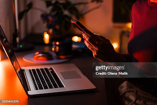 close-up of a woman using smartphone and laptop in dim lighting - dating app stock pictures, royalty-free photos & images