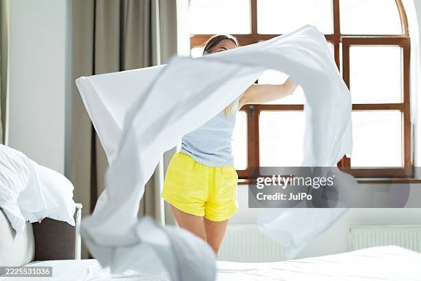 frau im mittleren erwachsenenalter, die morgens ihr bett macht - bettbezug stock-fotos und bilder