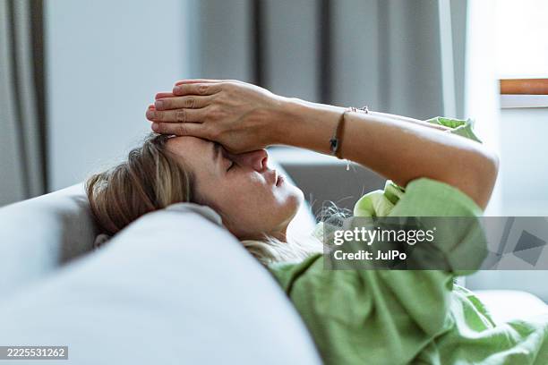 mid adult woman sitting on sofa in depression - headache stock pictures, royalty-free photos & images