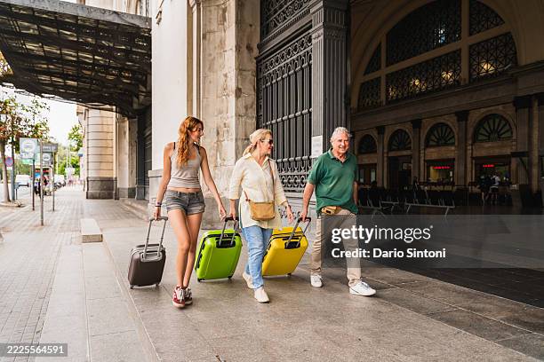 familie reist mit dem zug familie geht mit koffern aus dem bahnhof. generationenübergreifende verbindung und reise - rollkoffer stock-fotos und bilder