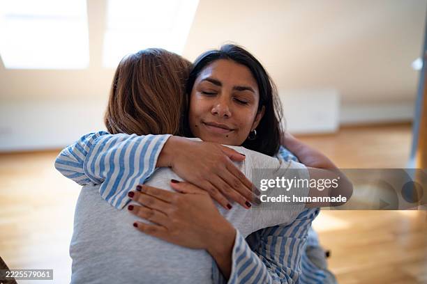 two young women are hugging at home with closed eyes - perdão imagens e fotografias de stock