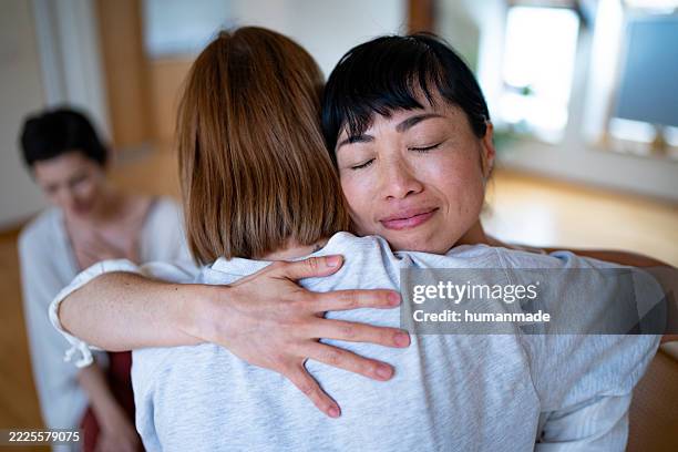 women are hugging and supporting each other during group therapy session - perdão imagens e fotografias de stock