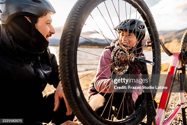 young cyclist helping his girlfriend fix bike during a ride in patagonia, argentina - bike tyre stock pictures, royalty-free photos & images