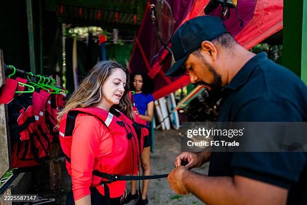 instructor helping a woman to put on a life jacket before aquatic sport - white water rafting stock pictures, royalty-free photos & images