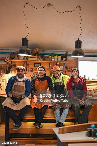 four carpenters smiling and posing in their workshop - handyman stock pictures, royalty-free photos & images