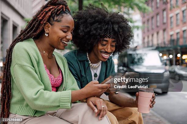 two friends in using mobile phone outdoors sitting on bench - couple texting stock pictures, royalty-free photos & images