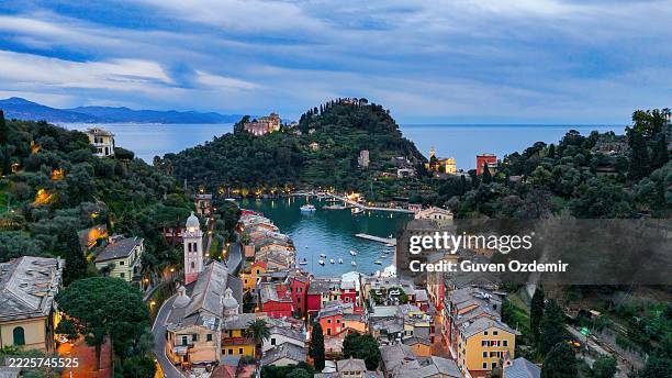 aerial view of portofino harbor at dusk with glowing lights, colorful historic buildings and calm sea, castello brown on the hill and mediterranean landscape, travel and romantic coastal town concept in italy - genoa italy stock pictures, royalty-free photos & images