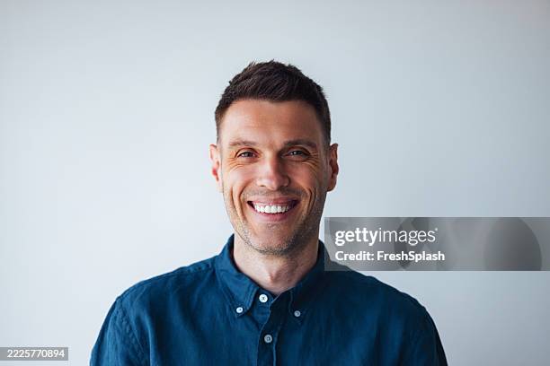 smiling man in blue shirt posing against clean white background - navy shirt stock pictures, royalty-free photos & images