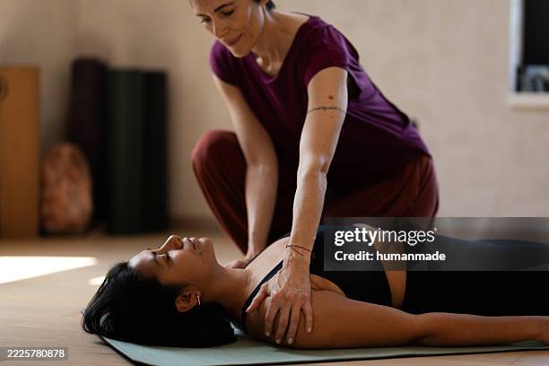 yoga teacher helping student performing restorative pose on mat - yoga instructor stock pictures, royalty-free photos & images