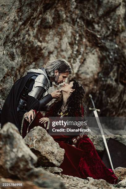black fantasy knight sitting on a rock above his queen gently holding her chin leaning in to kiss her - sword stock pictures, royalty-free photos & images