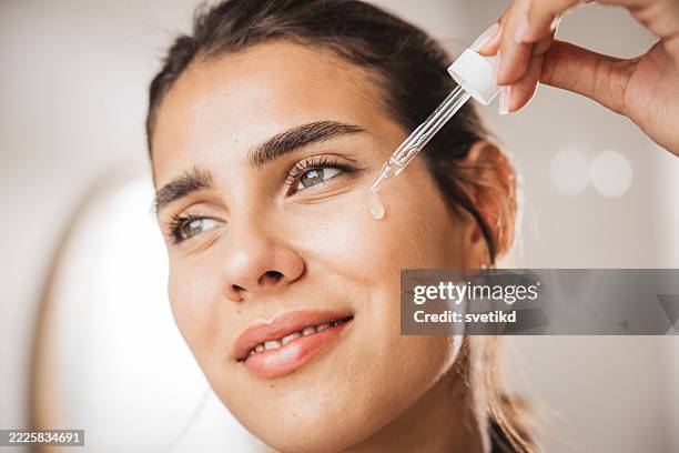 young woman applying serum on face - sérum de rosto imagens e fotografias de stock