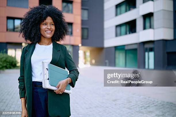 smiling businesswoman walking and holding digital tablet and folder in the city - green suit stock pictures, royalty-free photos & images