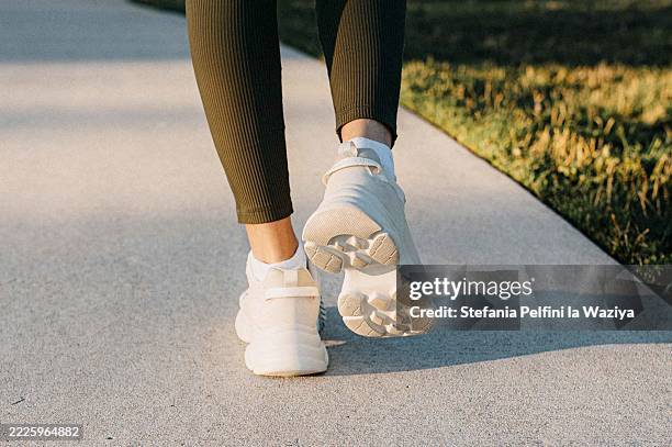 woman's feet walking on a sunlit pathway, wearing white sport shoes - paseo fotografías e imágenes de stock