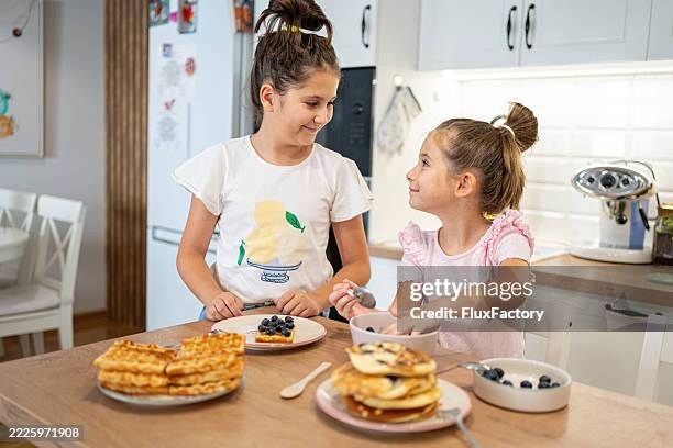 two children sharing a breakfast with blueberries in a bright kitchen - making waffles stock pictures, royalty-free photos & images