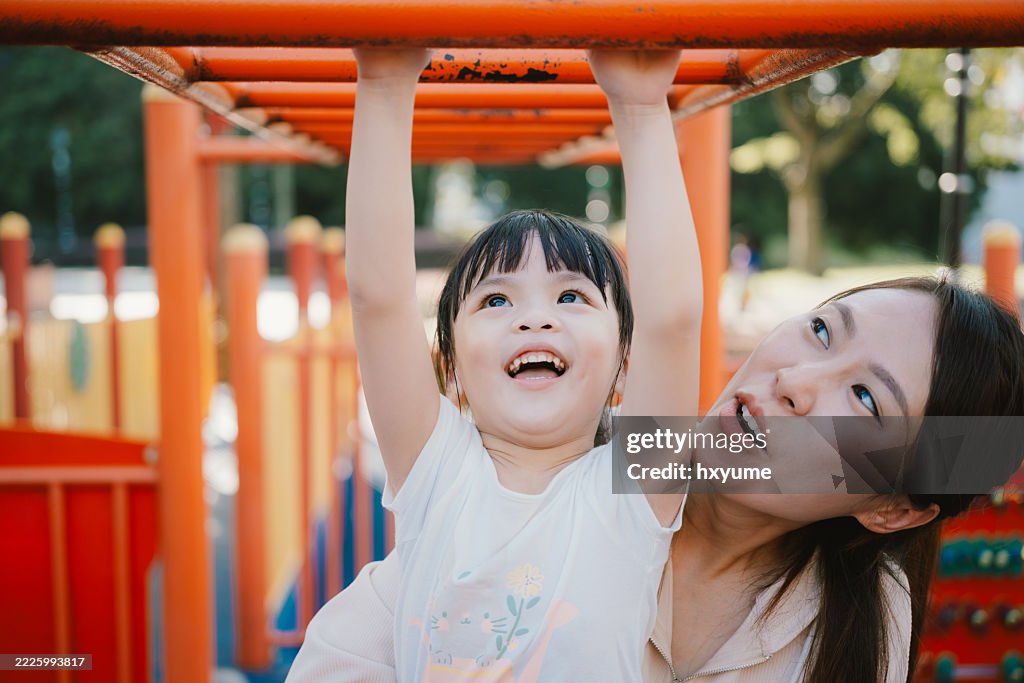 Asian Mother Helping Child Build Confidence on Monkey Bars