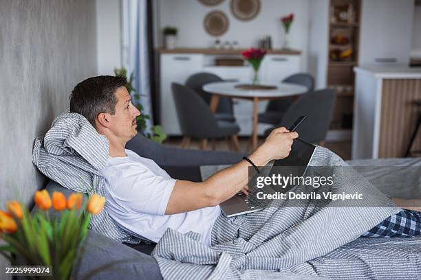 man working from home using laptop and smartphone on sofa - remote controlled stock pictures, royalty-free photos & images