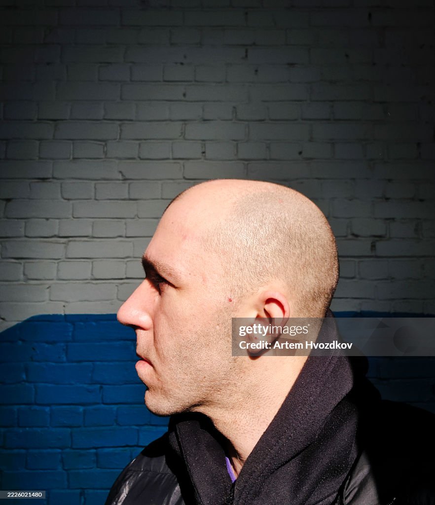 Serious bald man looking away with neutral facial expression against brick wall