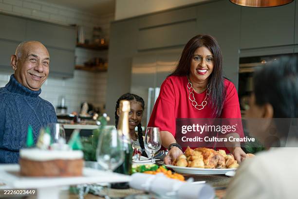smiling woman serving roasted turkey to family at table - indien dinde photos et images de collection